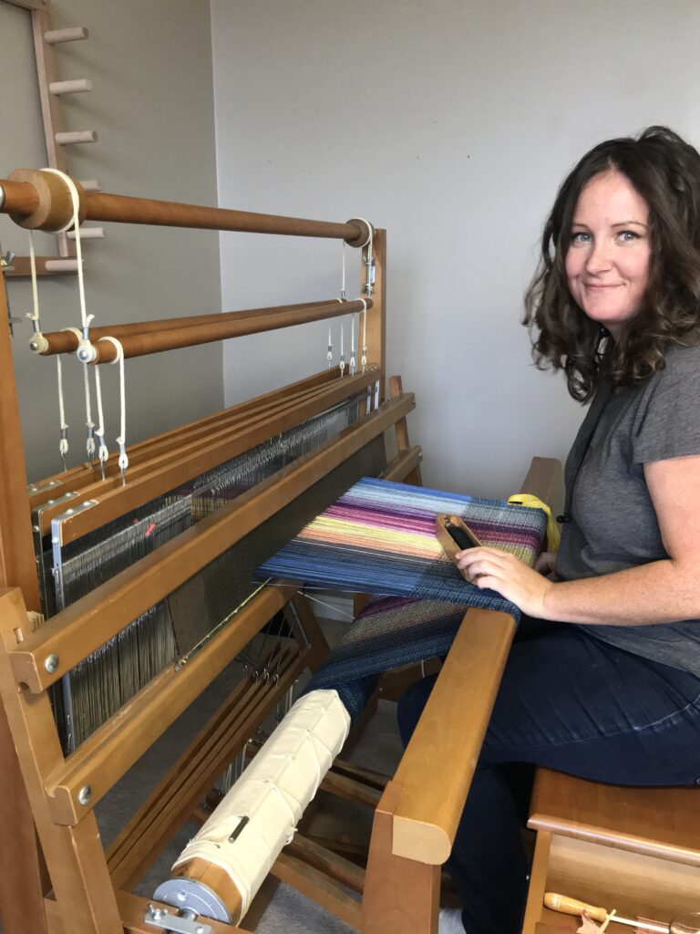 person sitting at a loom with a colourful warp